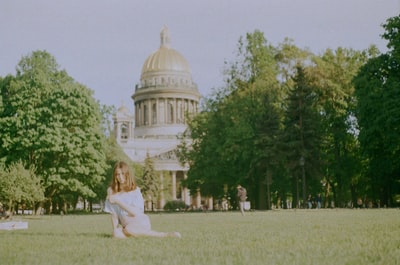 During the day, a woman dressed in white sitting near white dome building green grass
